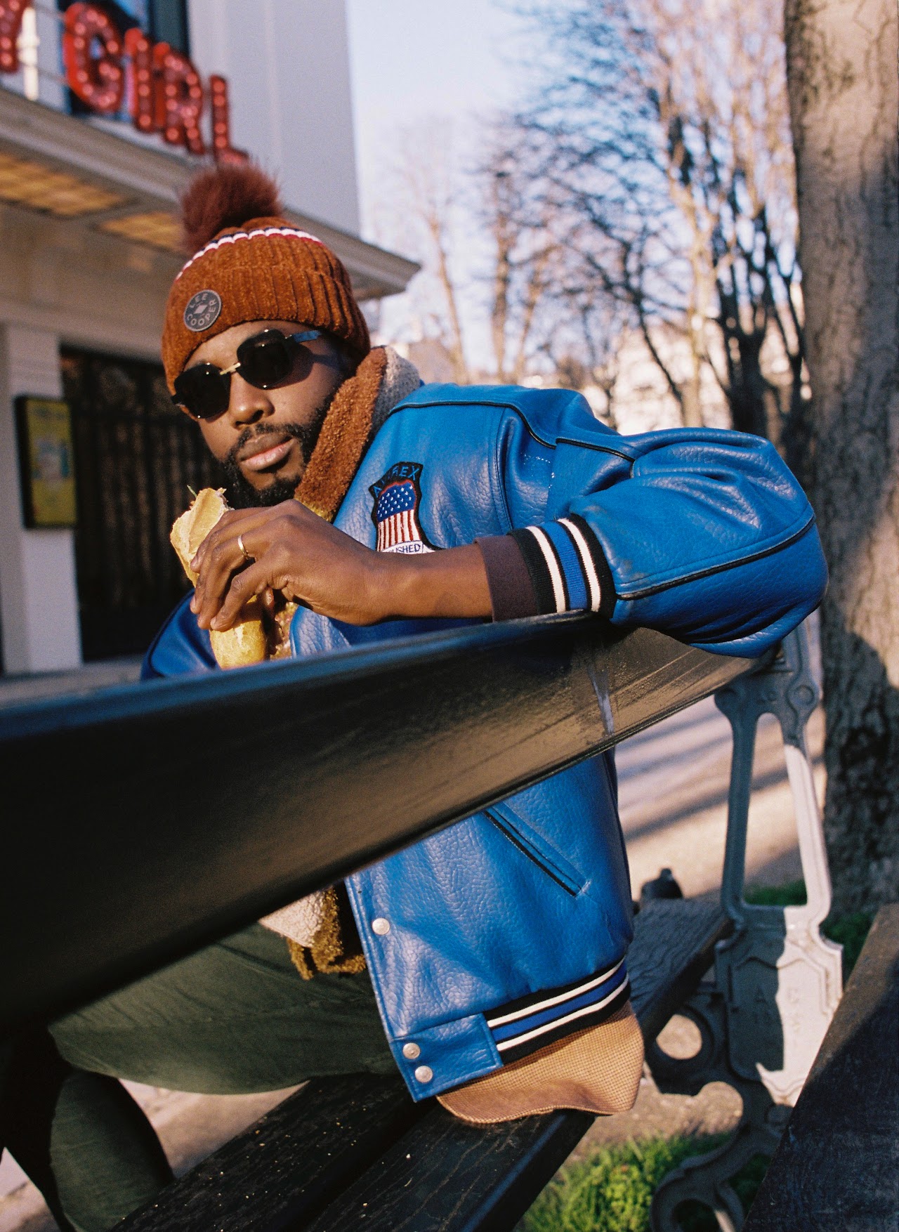 André accoudé à un banc, veste bleue et bonnet orange